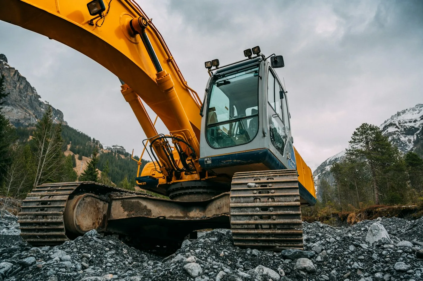 Tracked excavator on rocky ground beneath mountain terrain