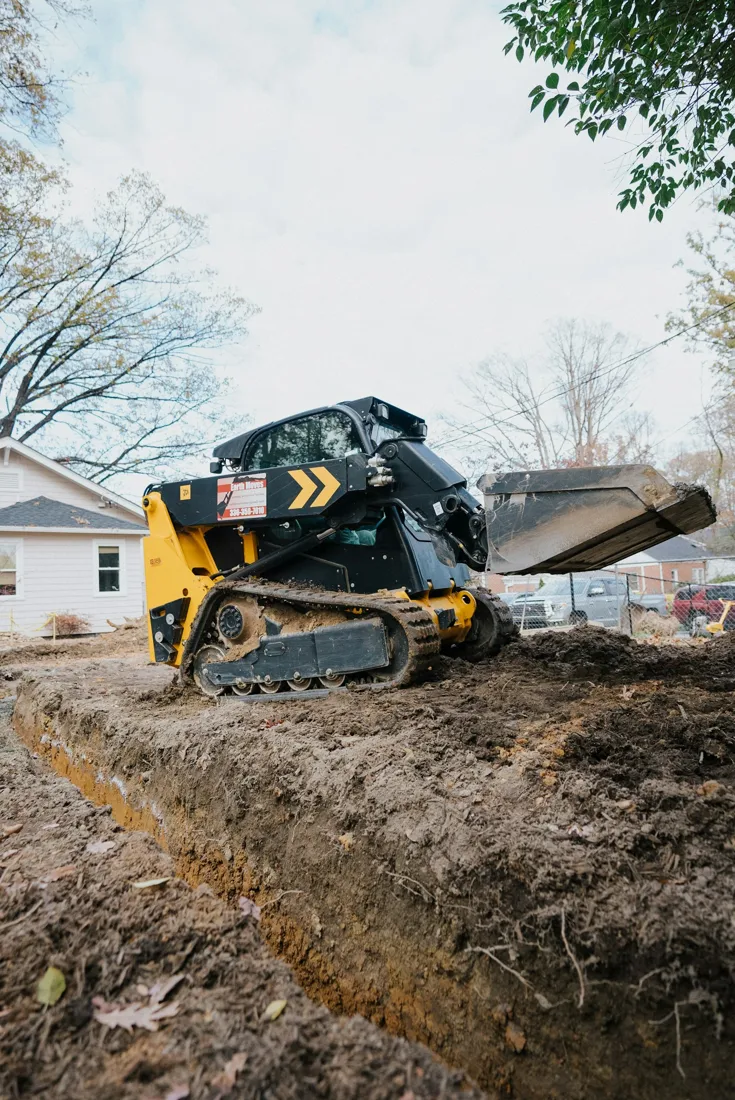 Compact tracked machine digging beside a house